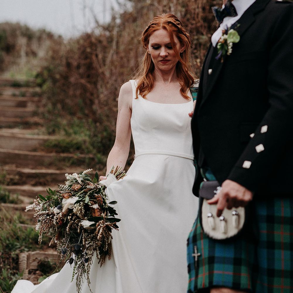 Bride in an April Ross wedding dress holding a foliage and anemone wedding bouquet by her side 