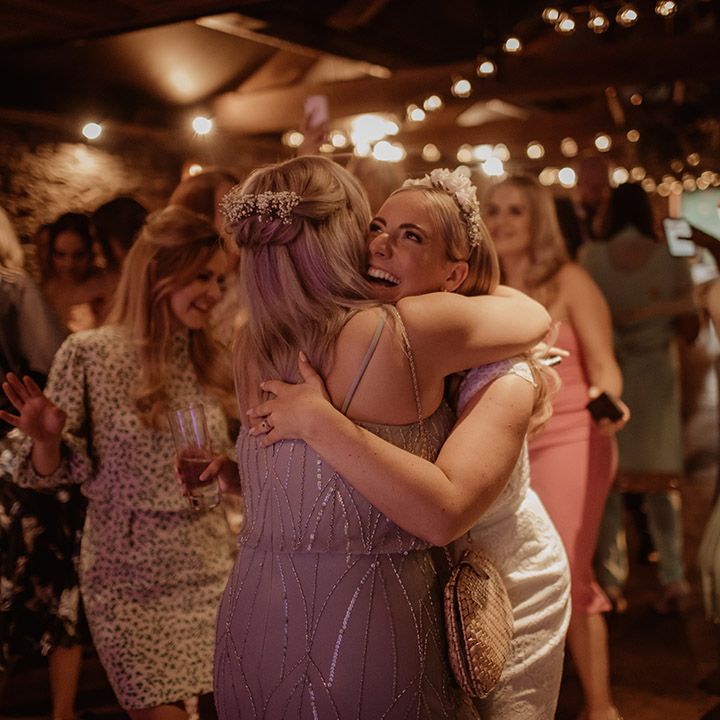 Bride in an appliqué headdress embracing a wedding guest on the dance floor 