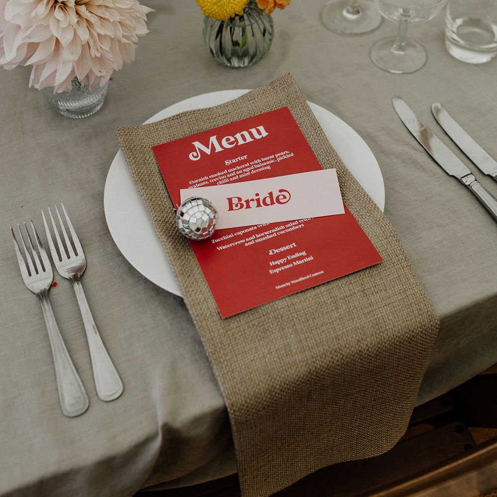 Place setting with burlap napkin, menu card, mini disco ball and flower stems in bud vases 