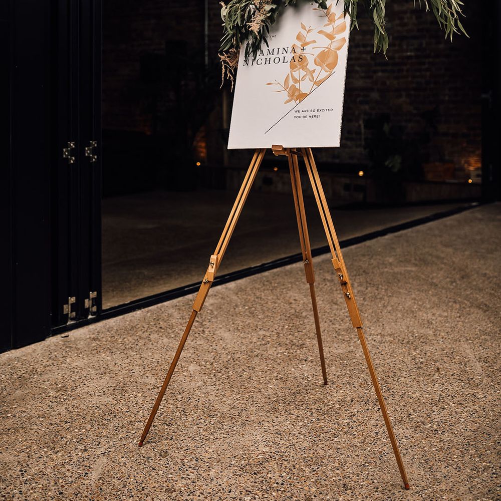 Wedding welcome sign with floral design and orange anthurium and green foliage decor on the wooden easel 