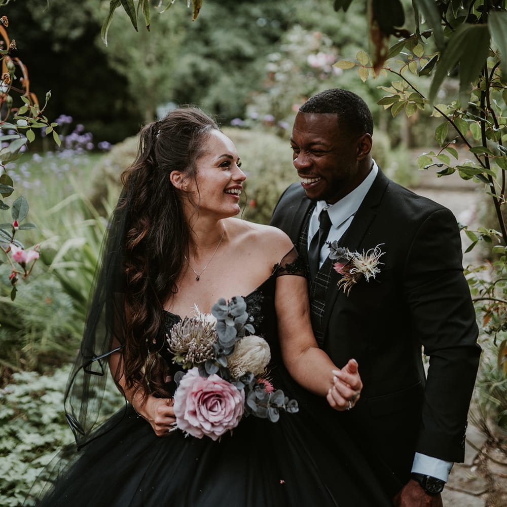 Bride looks lovingly at her groom as she holds pastel bouquet complete with green foliage