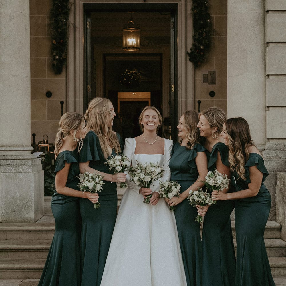 Bridal squad wearing Suzanne Neville, long white wedding dress and long bottle green dresses with black fur cropped coats
