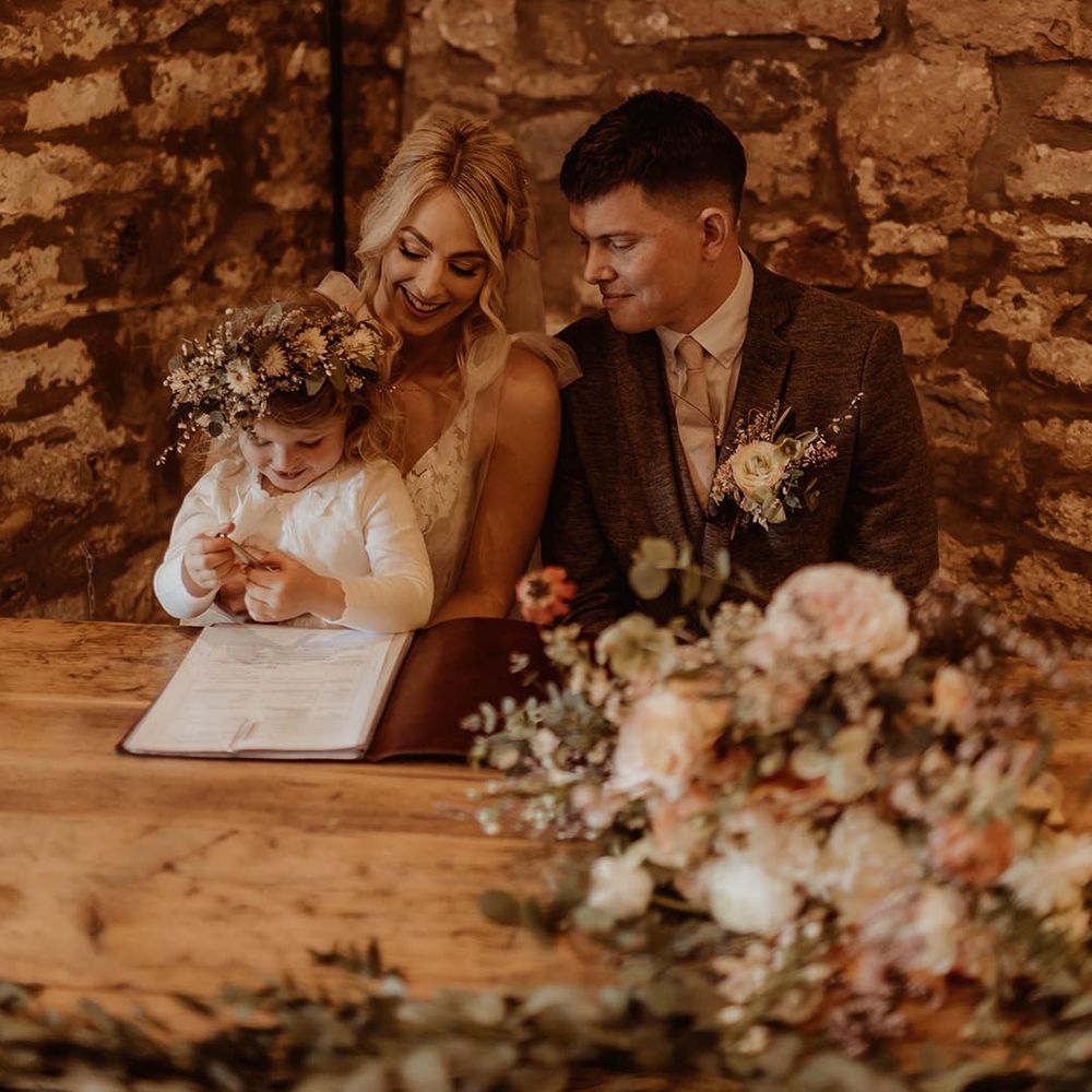 Bride and groom sign their wedding register with their daughter wearing a flower crown 