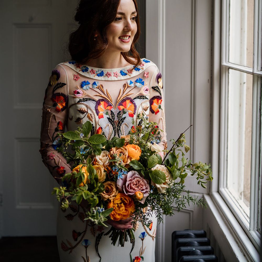 Bride in white wedding dress with bright and colourful flower detail with blue, orange and yellow bouquet