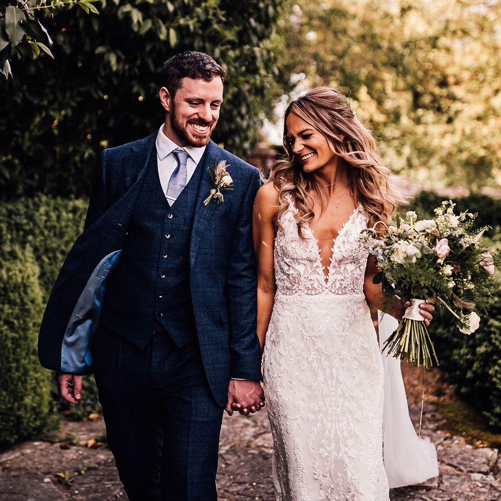 Groom in blue three piece suit and bride in lace v neck wedding dress walk together