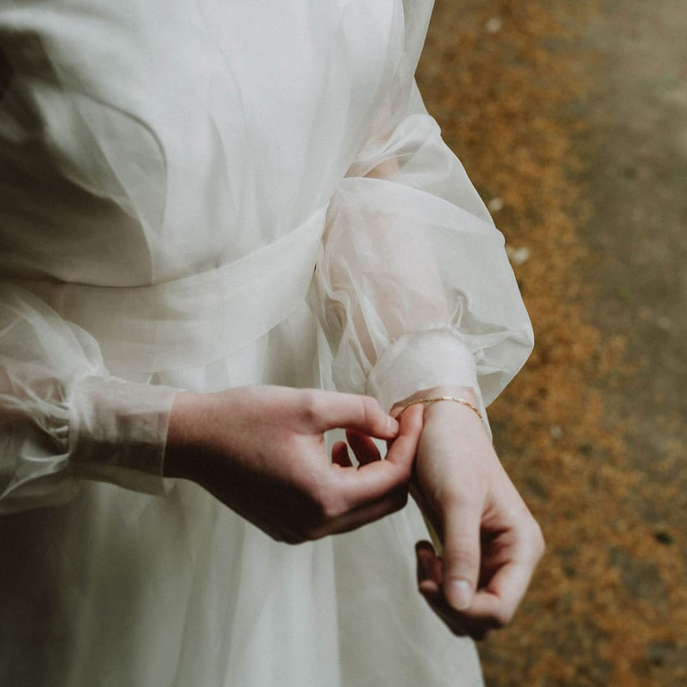 two layer sustainable fabric wedding dress with long sheer sleeves and delicate bridal necklace 