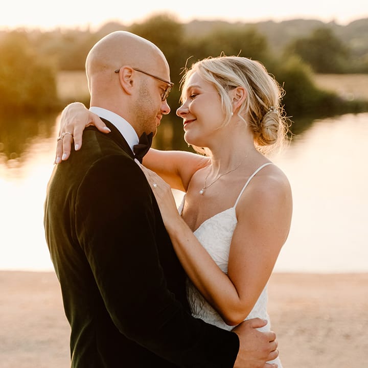 Bride wearing lace fitted wedding dress embraces her groom during golden hour at Bisham Abbey