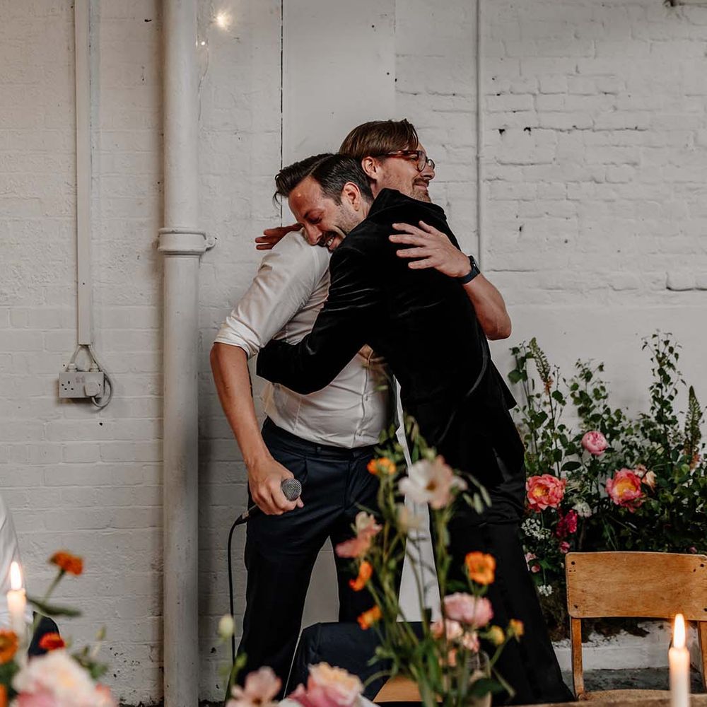 Groom in dark tux hugging wedding guest at Stylish Hackney Studios wedding