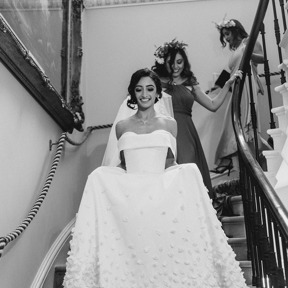 Bride walks down the stairs in bespoke Emma Beaumont design wedding dress with off the shoulder styling 