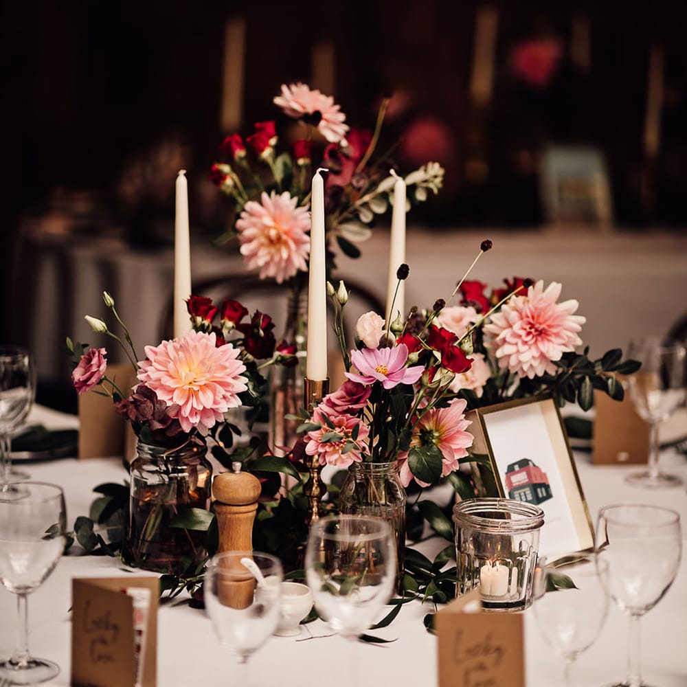 Bud vases full of pink and red wedding flowers and white taper candles for the centrepieces 