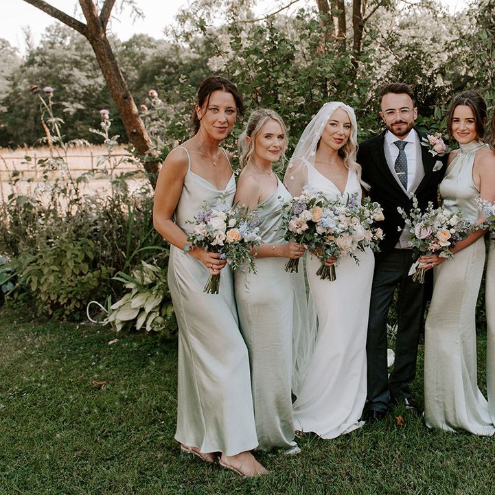 Groom in three piece suit with the bride in a Made With Love wedding dress with bridesmaids in sage green dresses in mismatched styles 