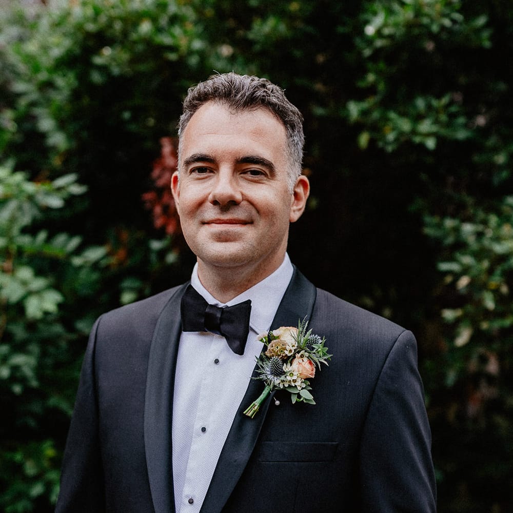 Groom in black tuxedo wearing a pink rose and thistle buttonhole 