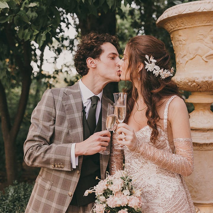 bride in a sparkly gold wedding dress with detachable sleeves kissing her groom in a grey check suit 