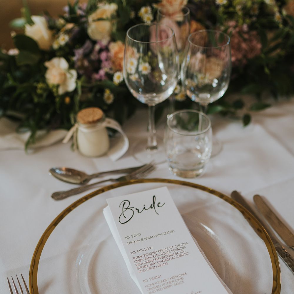 Black and white wedding menu stationery on clear charger plates with gold rim for classic and neutral wedding tablescape 