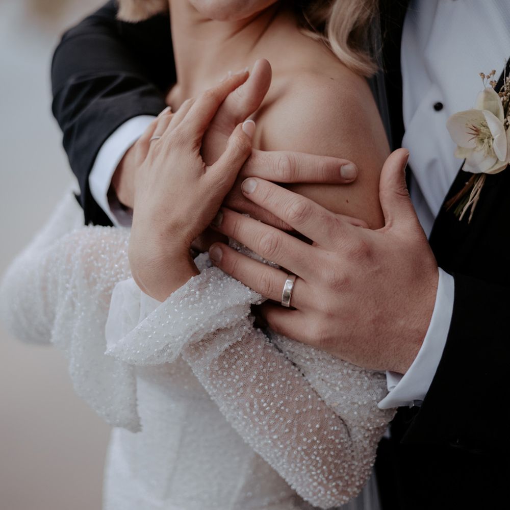The groom wearing a think silver wedding band giving the bride and intimate embrace on their wedding day 