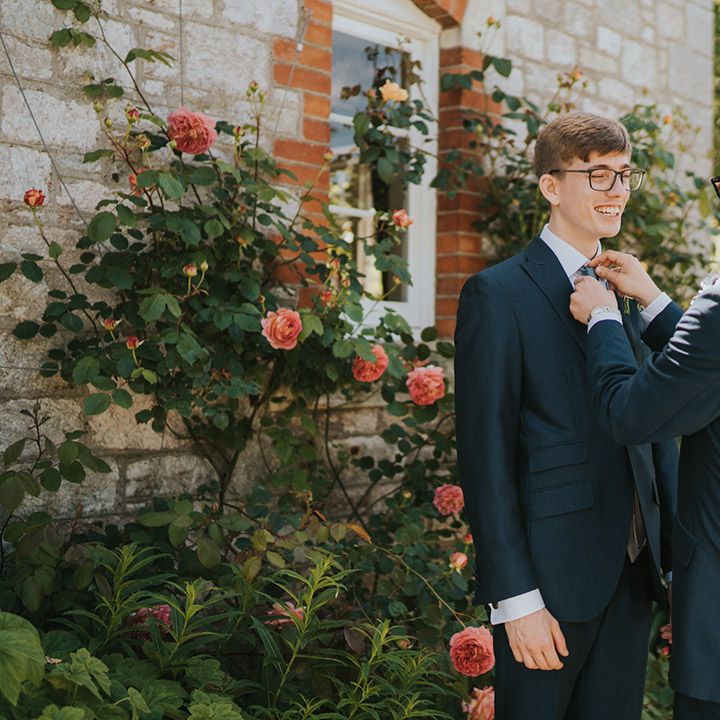 The groomsman helps the groom with the finishing touches for his wedding outfit by fixing on the buttonhole 