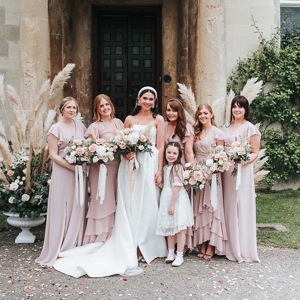 Bride in strappy satin wedding dress with puddle train standing with bridesmaids in ruffle short sleeve pink bridesmaid dresses 