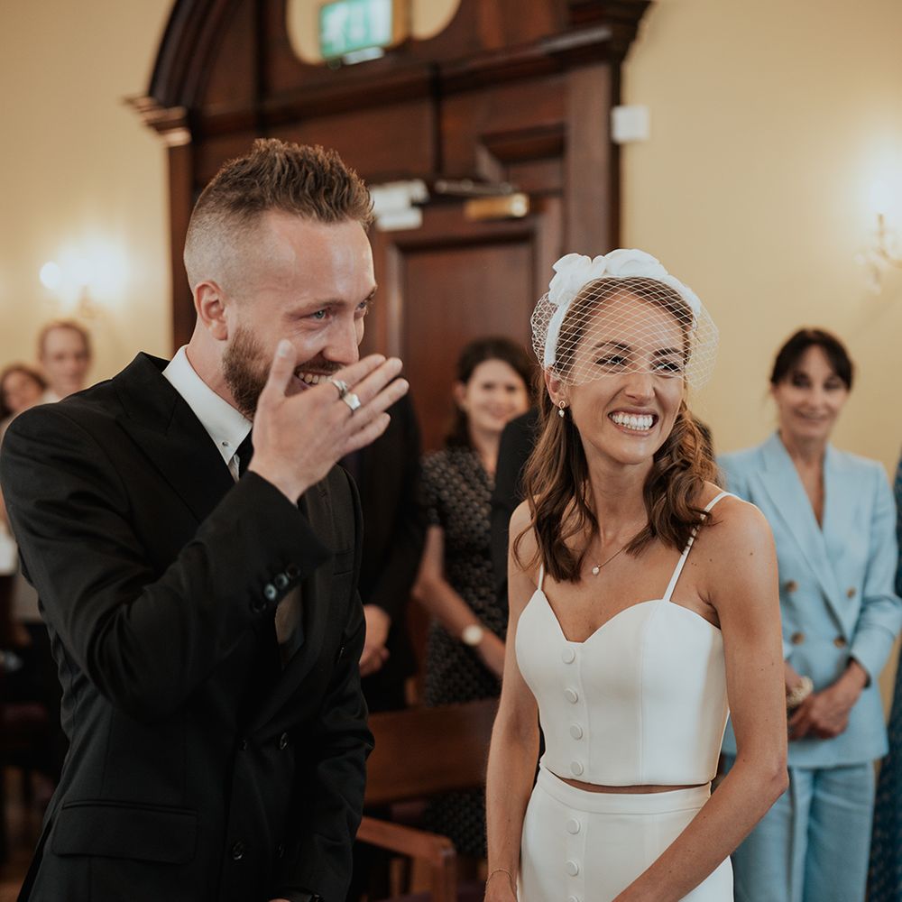 groom in a black suit laughing during the Chelsea town hall registry office wedding ceremony 