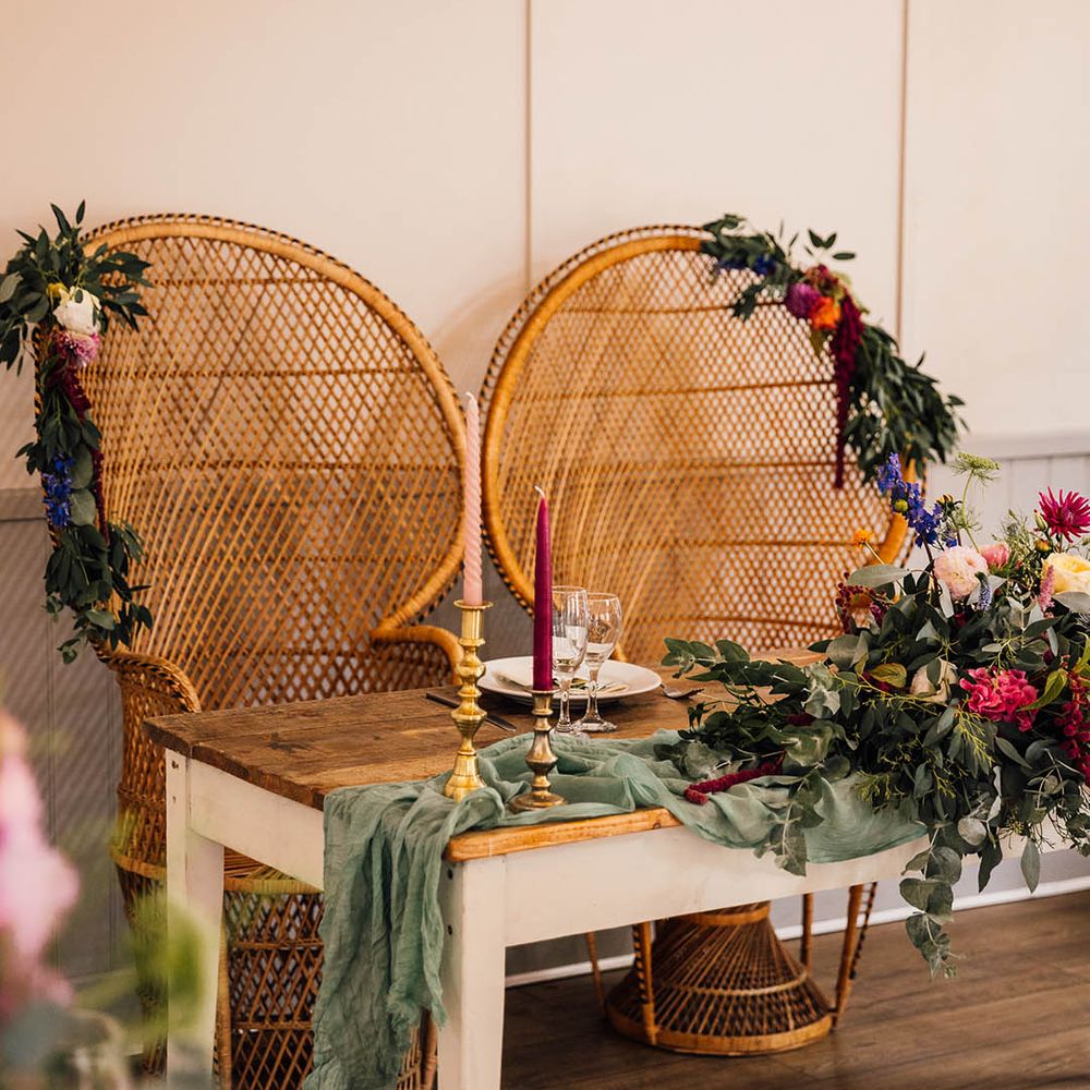 Sweetheart wedding table with two boho peacock chairs with foliage decor and colourful flowers 