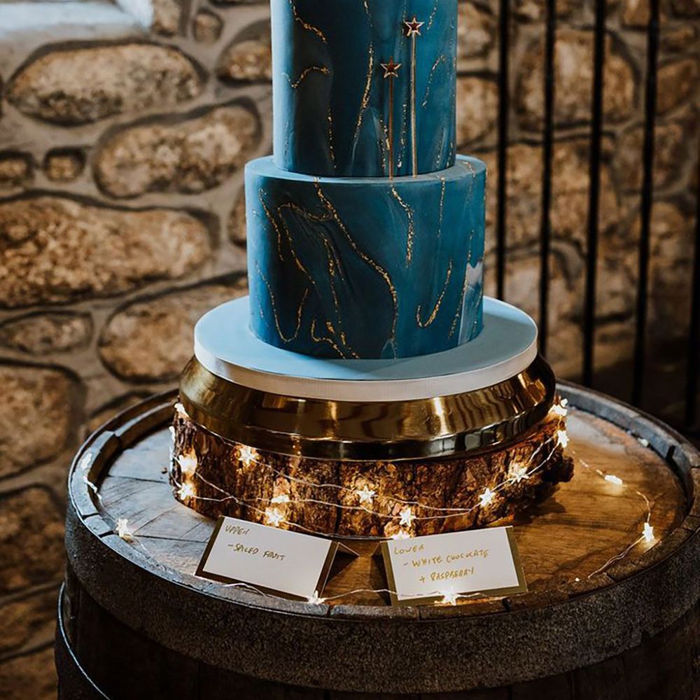 Two tier navy blue iced wedding cake with shimmery gold detailing and crescent moon cake topper for celestial wedding 
