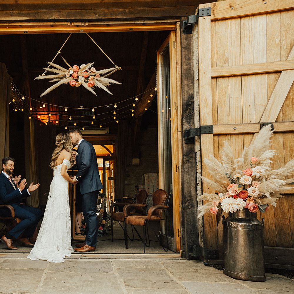 Bride and Groom kiss under pampas grass and rose flower cloud