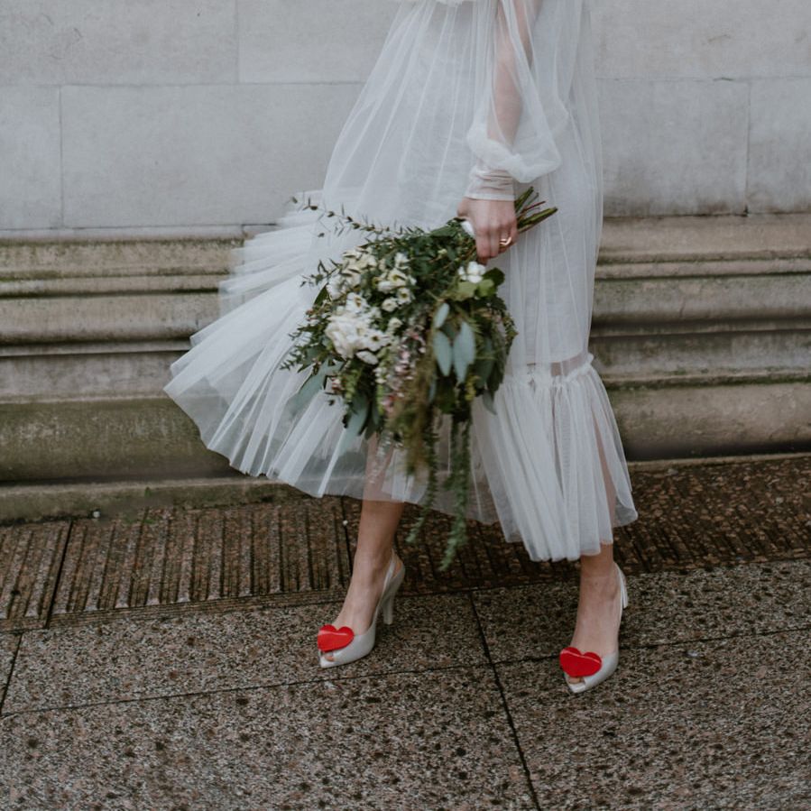 Bride in a tulle midi dress with long sleeves and high neck holding a green and white bouquet and wearing Vivienne Westwood shoes 