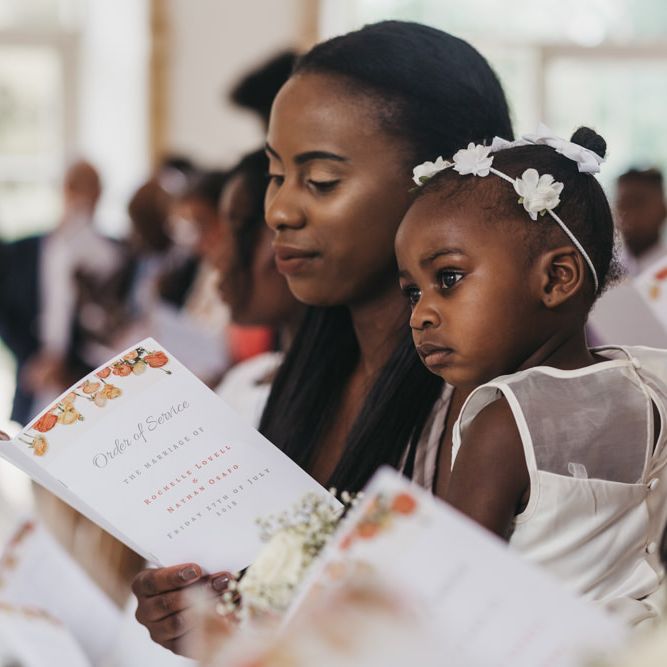 Bridesmaid holding a DIY order of service and a flower girl with flower headdress