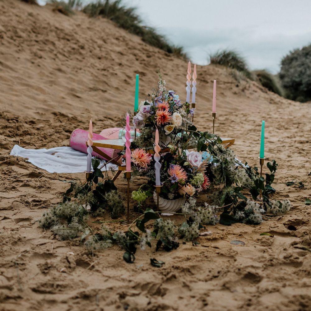 Twisted colourful candles in gold candlestick holders and pastel flower arrangements for intimate picnic on the beach 