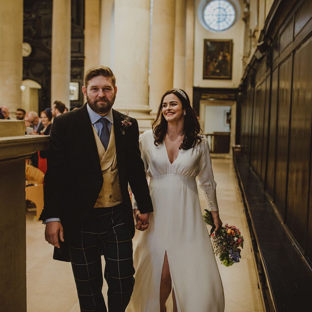 Bride and groom holding hands after getting married groom wears tartan trousers, bride wears long sleeve wedding dress