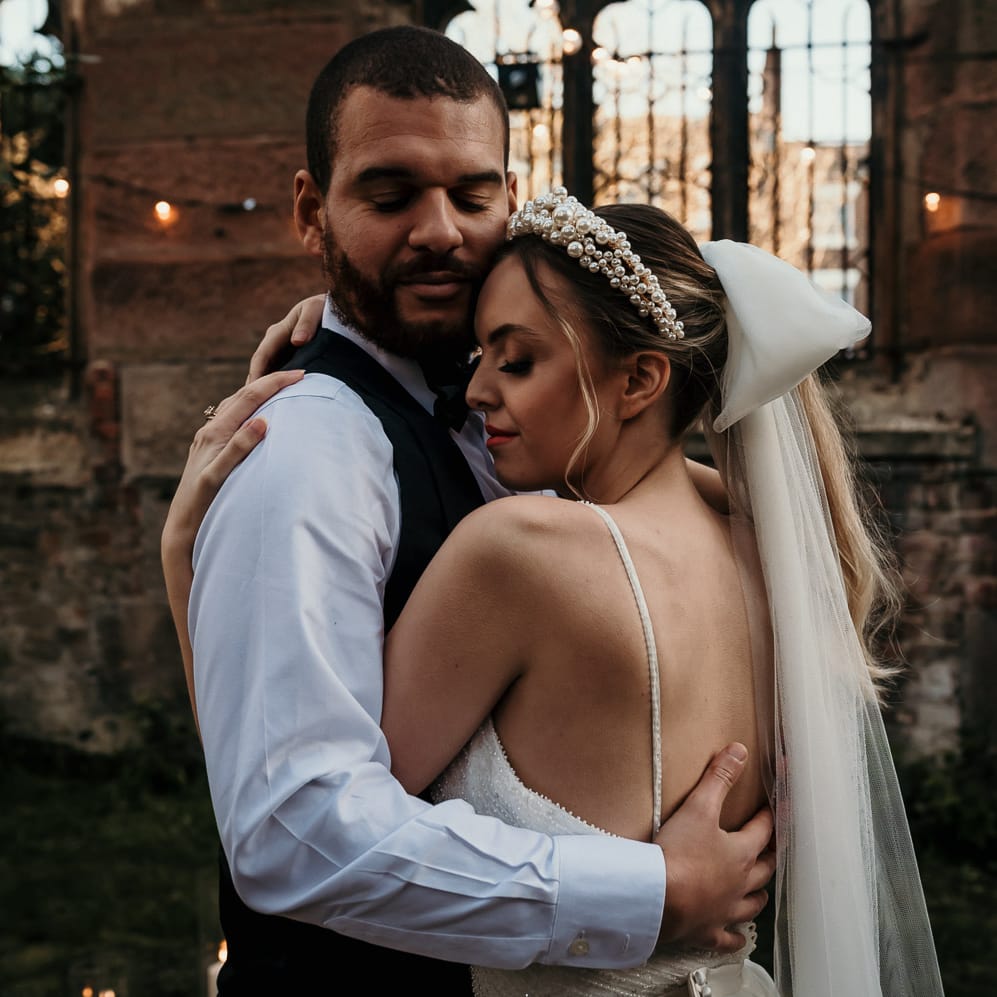 Bearded groom embracing his bride wearing a pearl headband and bow wedding veil 
