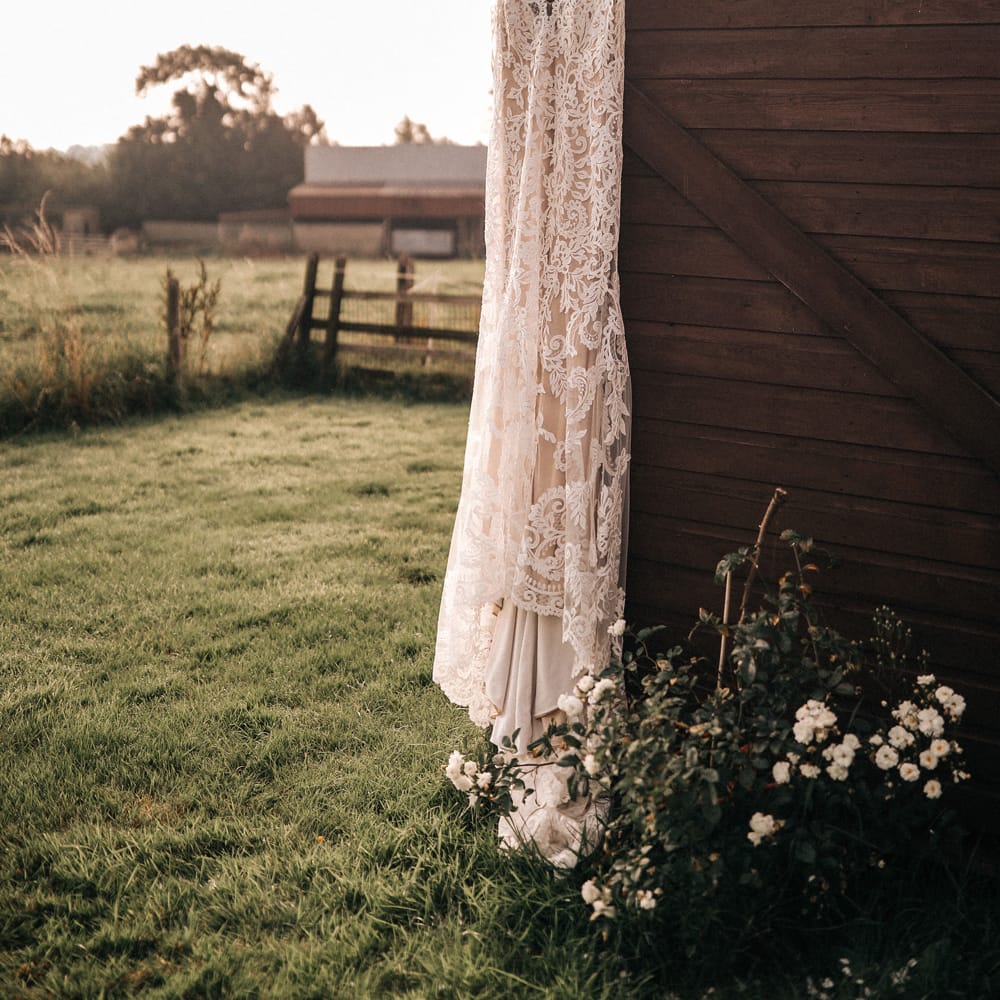 A lace boho wedding dress hangs from a wooden structure. 