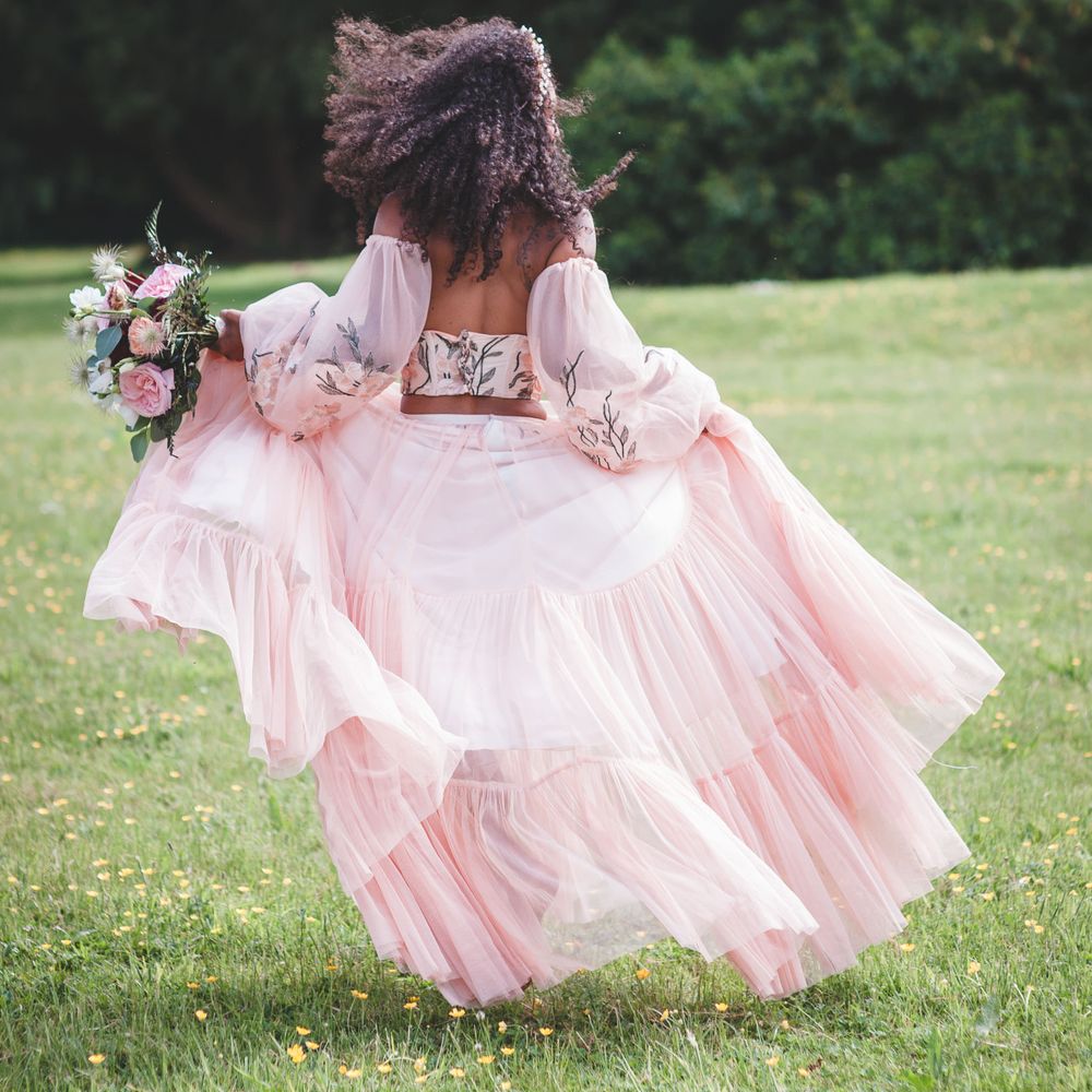 black bride with long naturally curly hair running in a garden in blush pink bridal separates with tulle skirt, embroidered bodice and detachable sleeves 