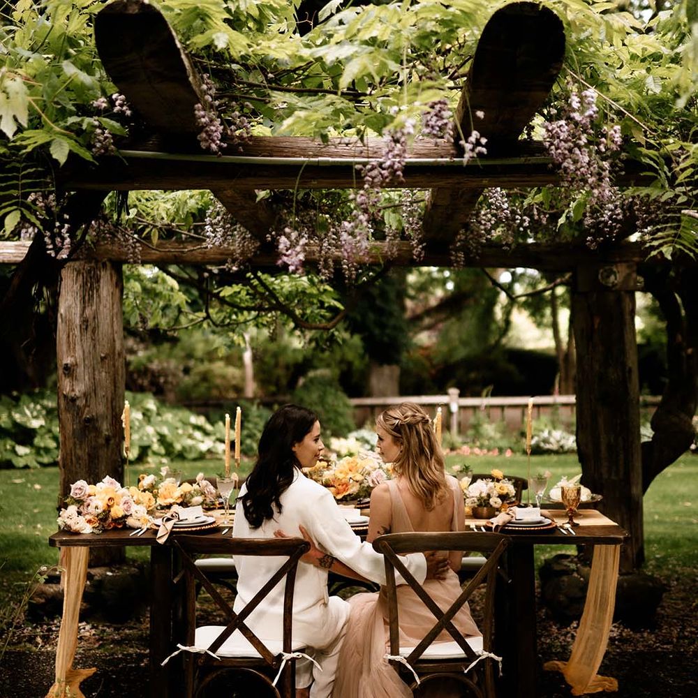 Two brides sitting at their outdoor wedding reception with honey yellow wedding decor 