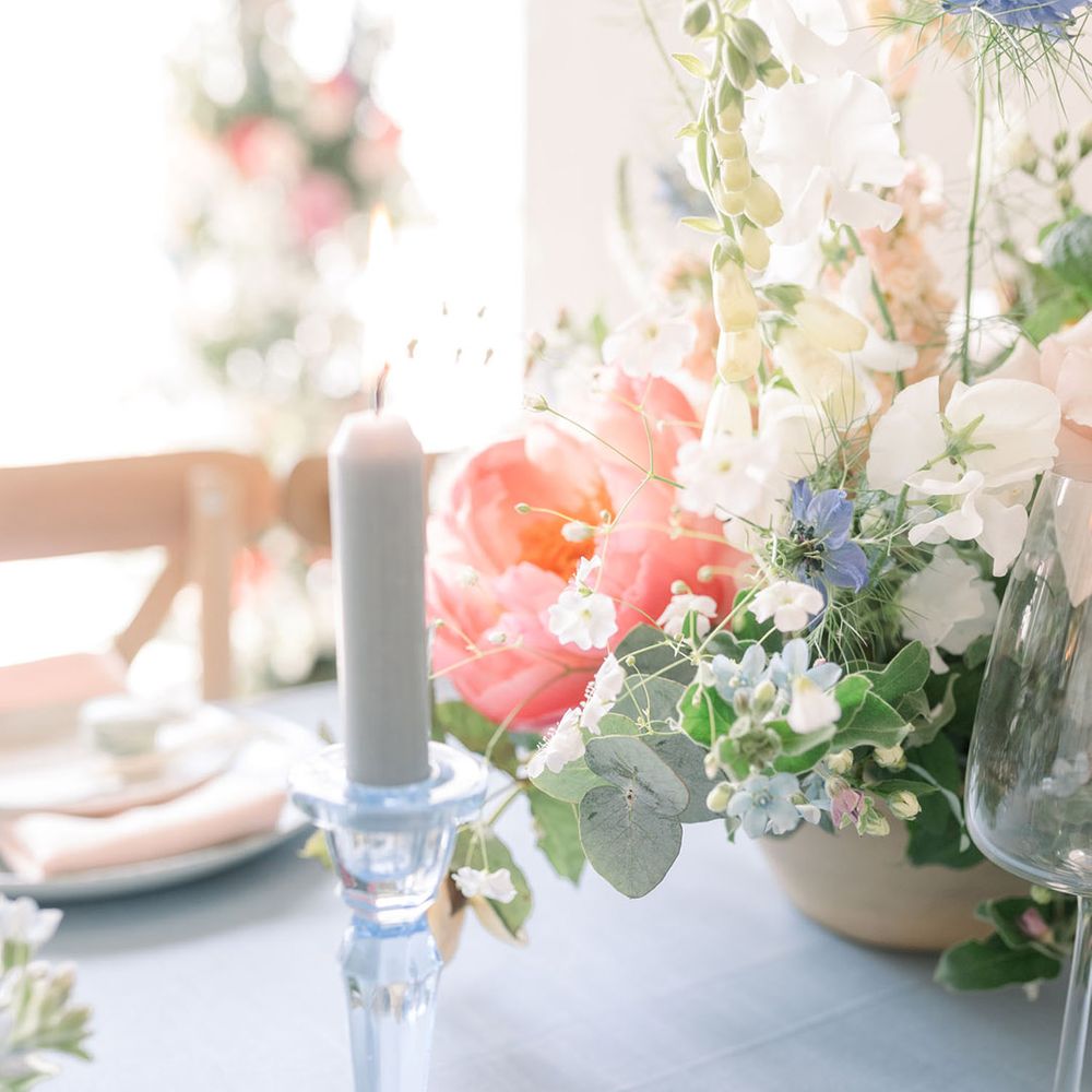 Blue taper candle in a crystal candlestick holder against a pastel flower centrepiece decoration 