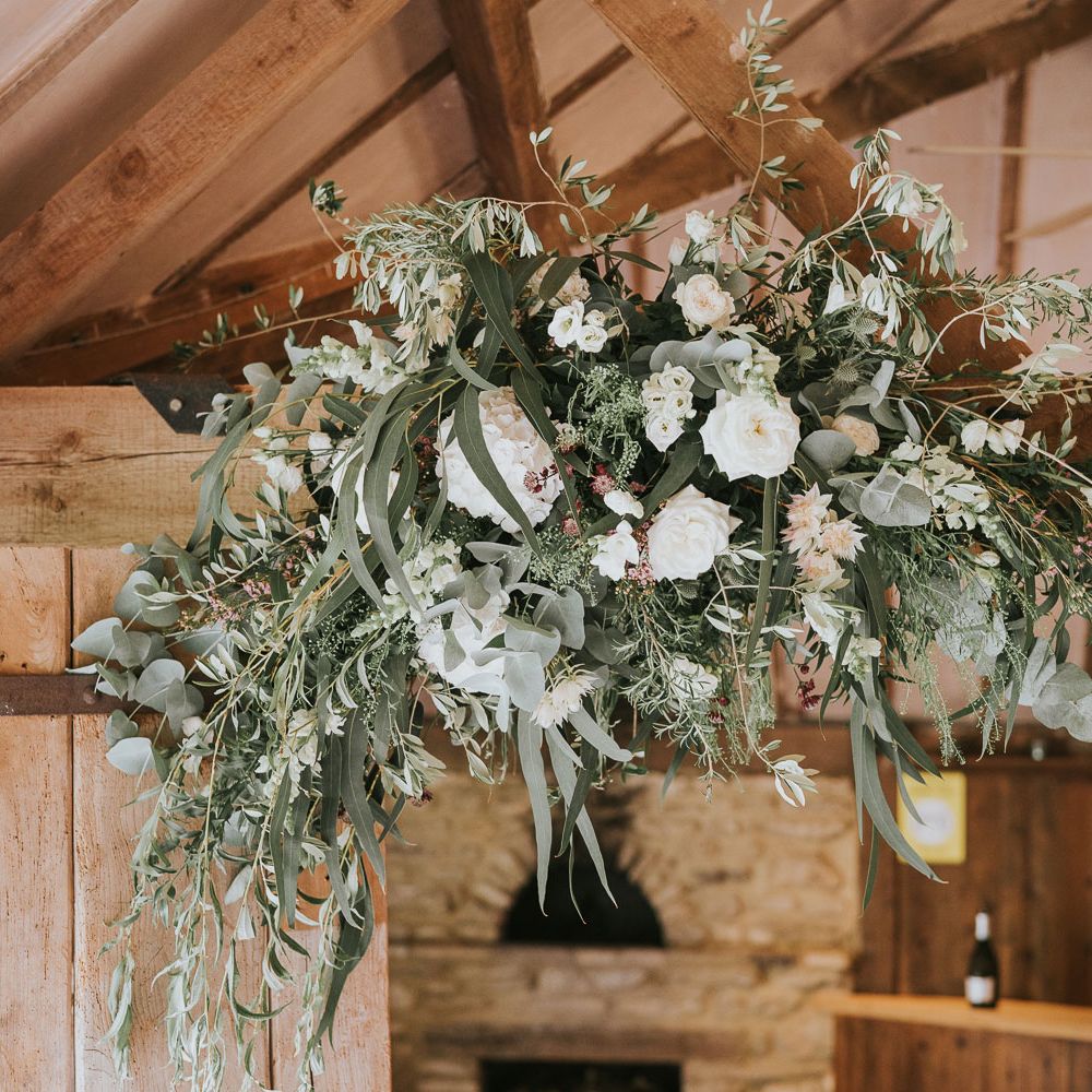 White, green and pink flower cloud hung from wooden beam at Tythe Barn wedding with barn wedding flowers
