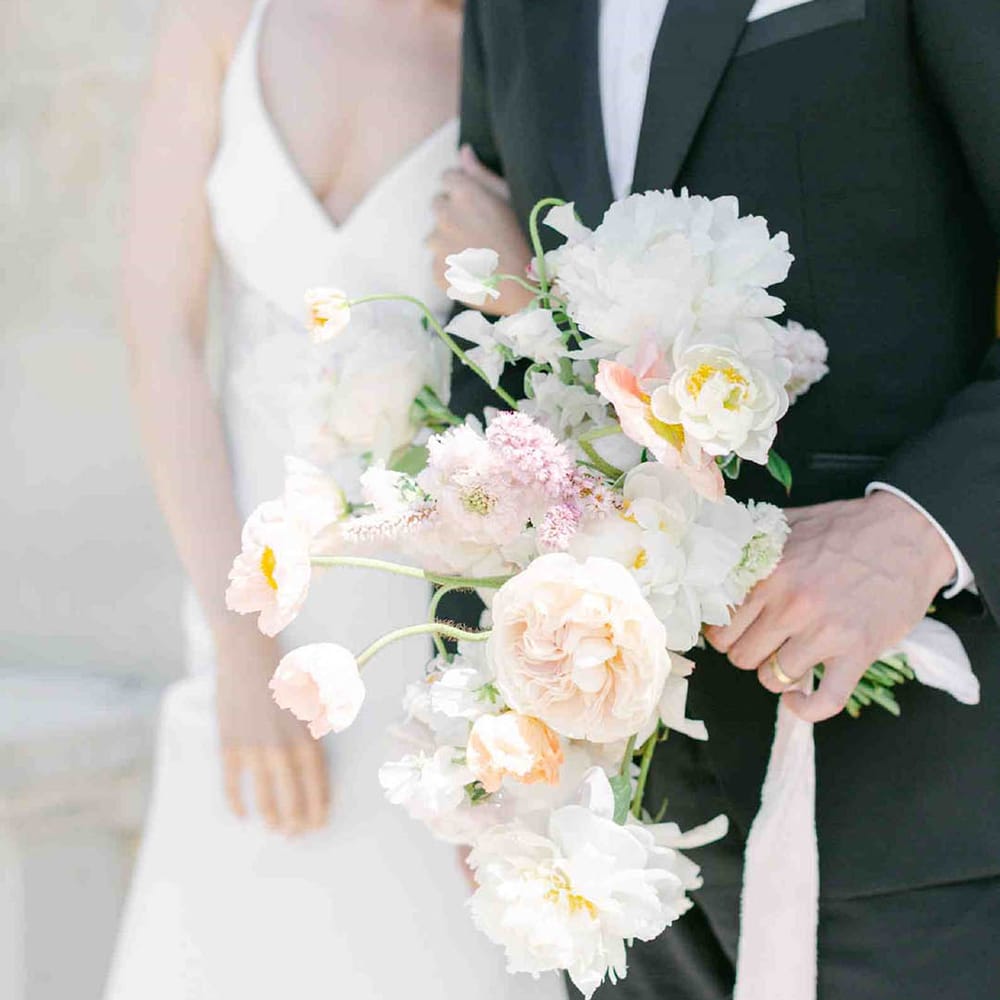 Groom holding a pastel flower wedding bouquet with roses, peonies, Icelandic poppies, sweet peas, scabious, foxglove, and snapdragons