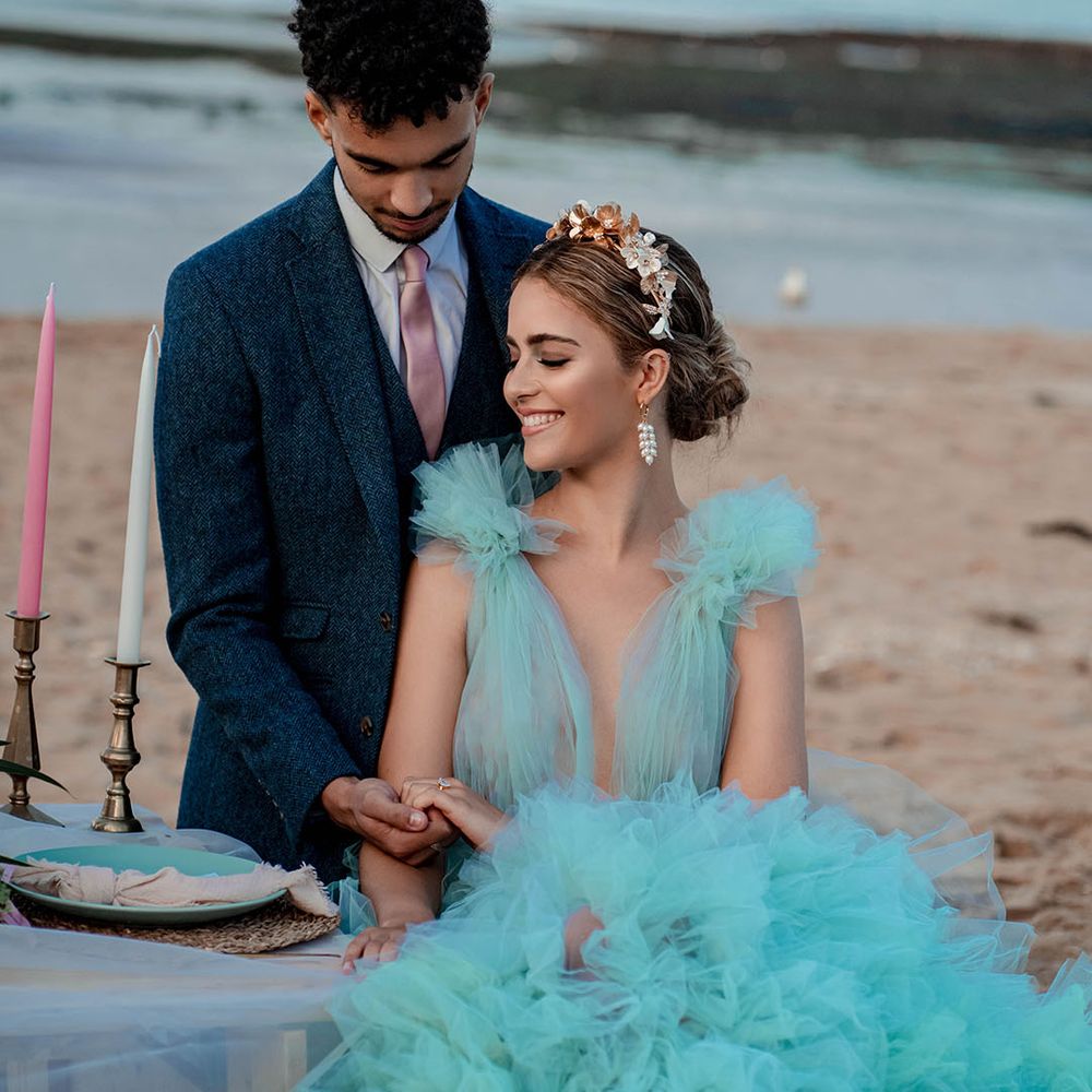 Beautiful bride with pinned updo and gold headband wearing a mint green wedding dress holding hands with there groom in a blue wool suit at their coastal beach elopement 