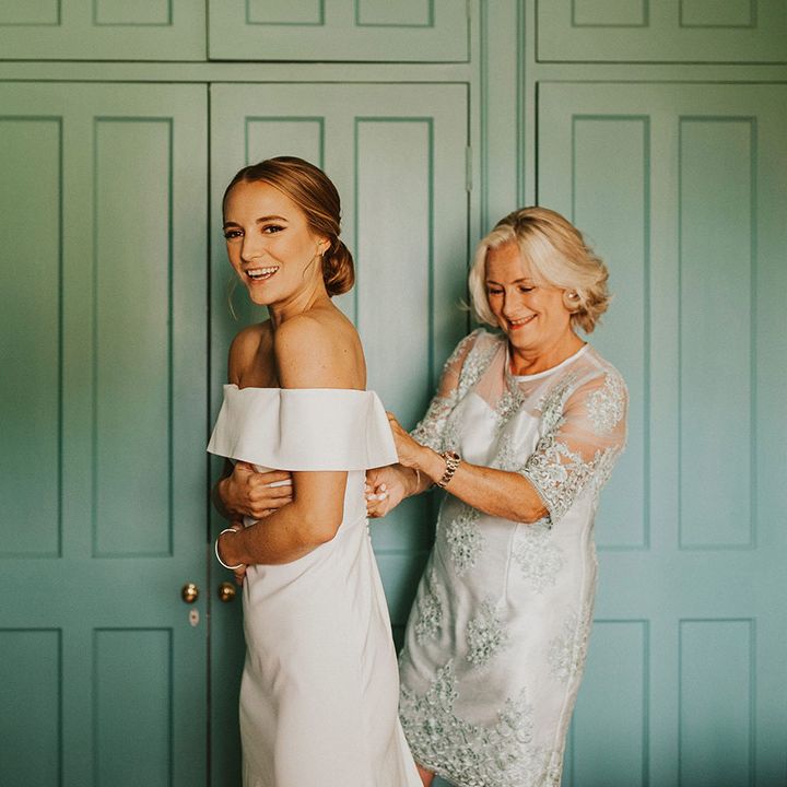 Mother of The Bride does up wedding gown for bride who wears off the shoulder wedding gown and hair pulled back into low bun