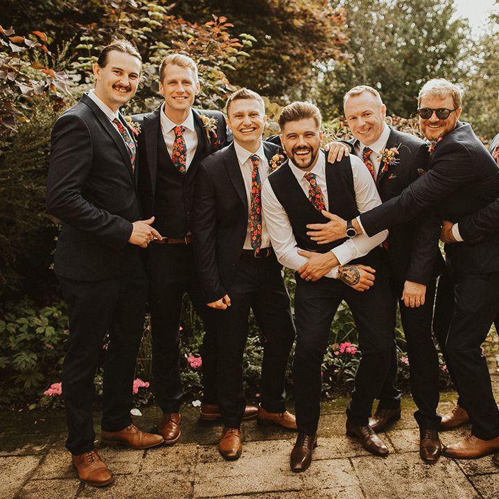 Groom and groomsmen in navy suits with floral Liberty print ties at back garden wedding 