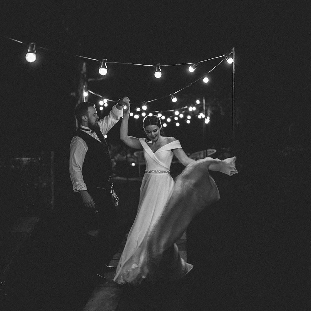 groom twirling his bride in a Suzanne Neville wedding dress under a canopy of festoon lights 