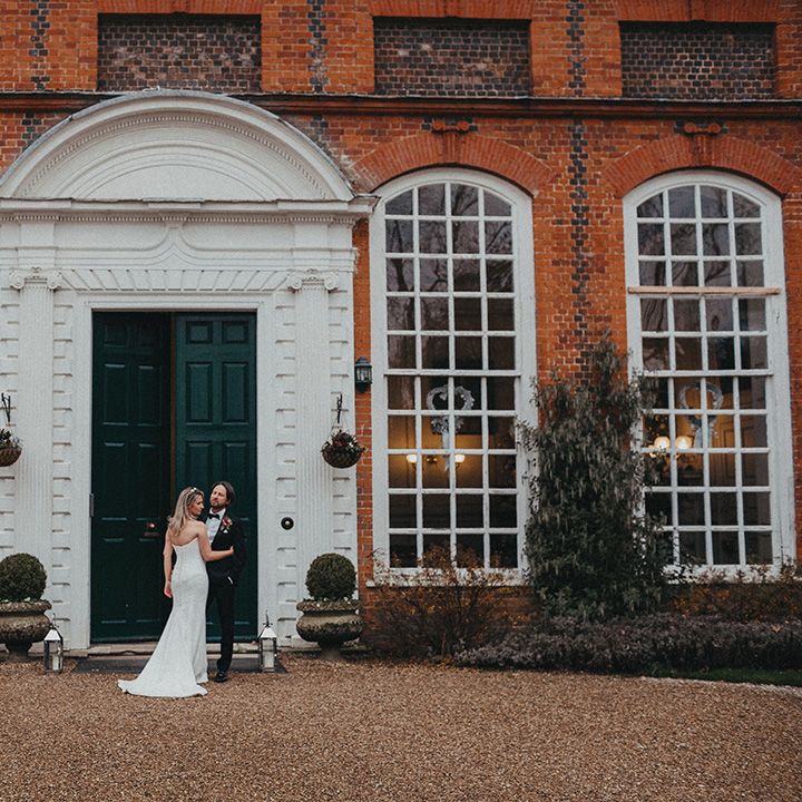 Bride & groom stand in front of green door on their wedding day at Gosfield Hall 