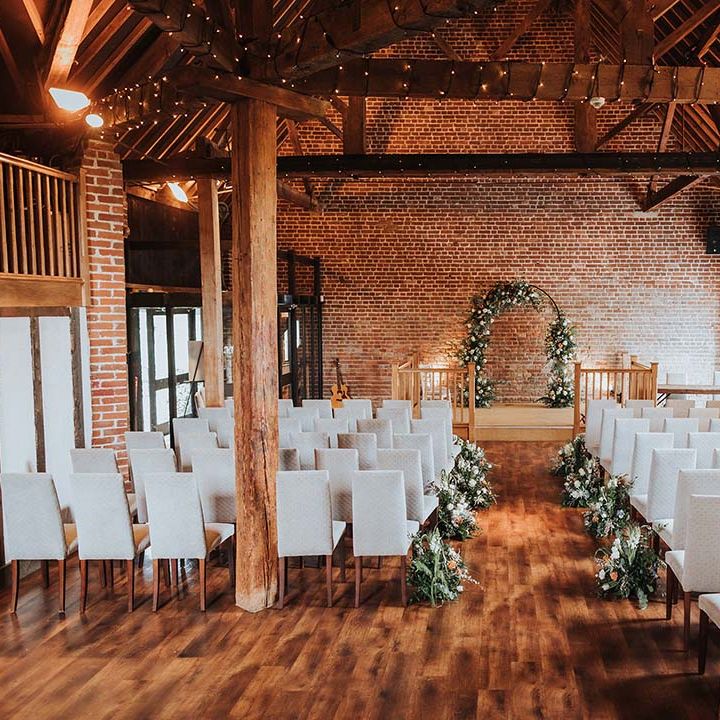 Rustic barn wedding venue in Kent with white tall back chairs and fairy lights