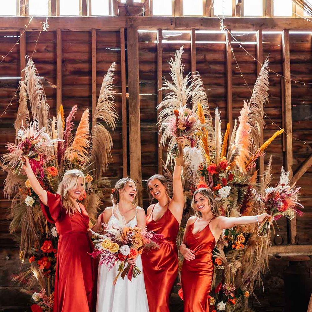 bridal party in burnt orange satin bridesmaid dresses, bride in floor length strappy wedding dress 