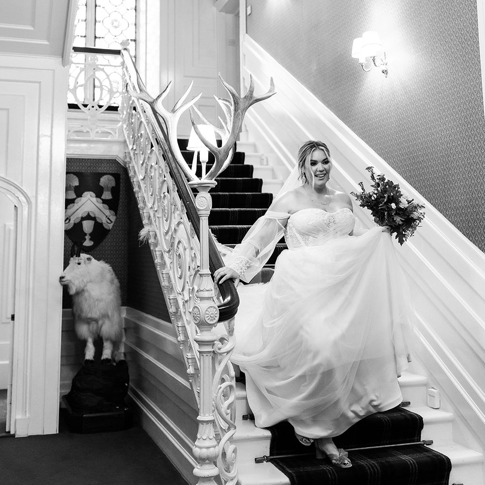 Bride in strapless wedding dress with sheer sleeves descends the stairs at castle wedding venue