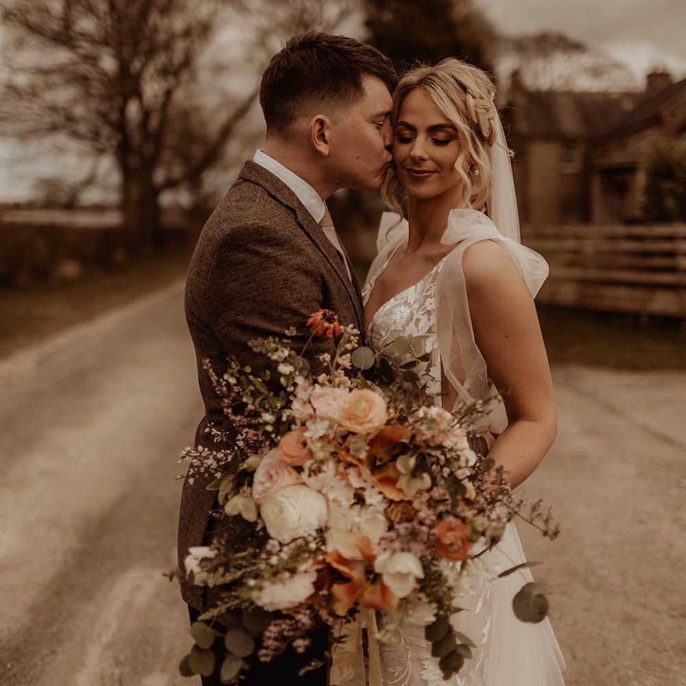 Groom kisses the bride on the cheek after their barn wedding ceremony with bride wearing Made With Love Elsie dress