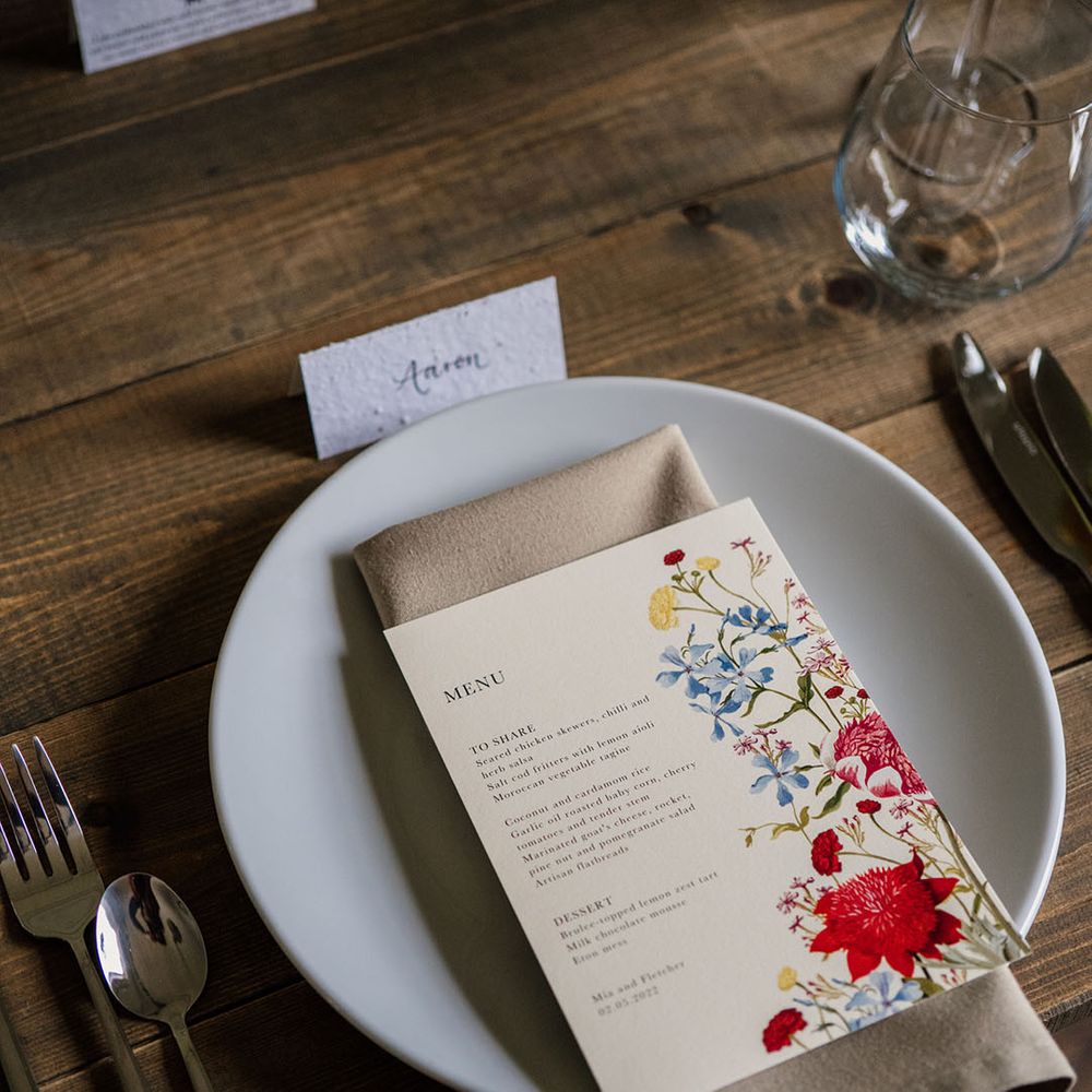 White plate and beige napkin with white menu card decorated with bright flower design 