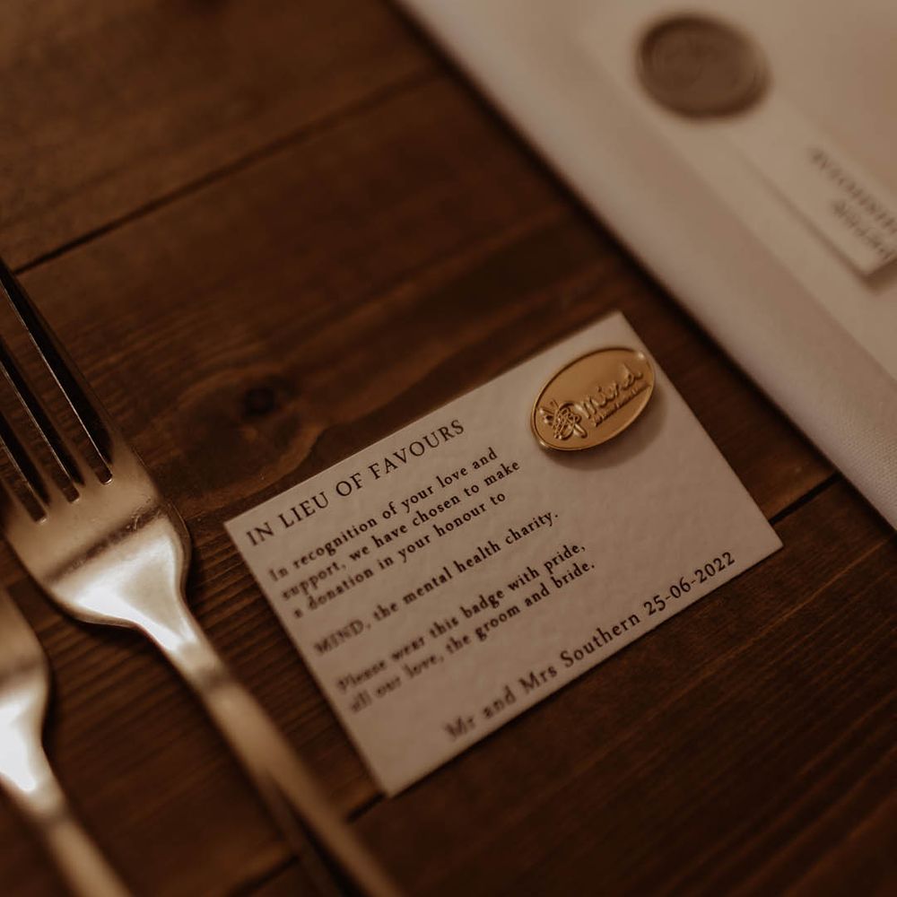 Small card with gold pin attached for Mind mental health charity where the couple made donations to instead of wedding favours