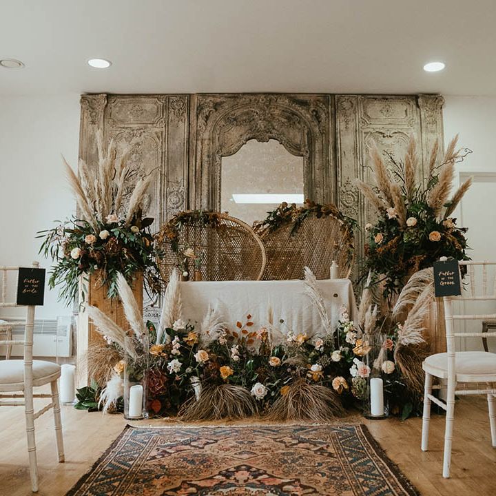 Altar decorations with pampas grass, peacock chairs and pillar candles in hurricane vases 