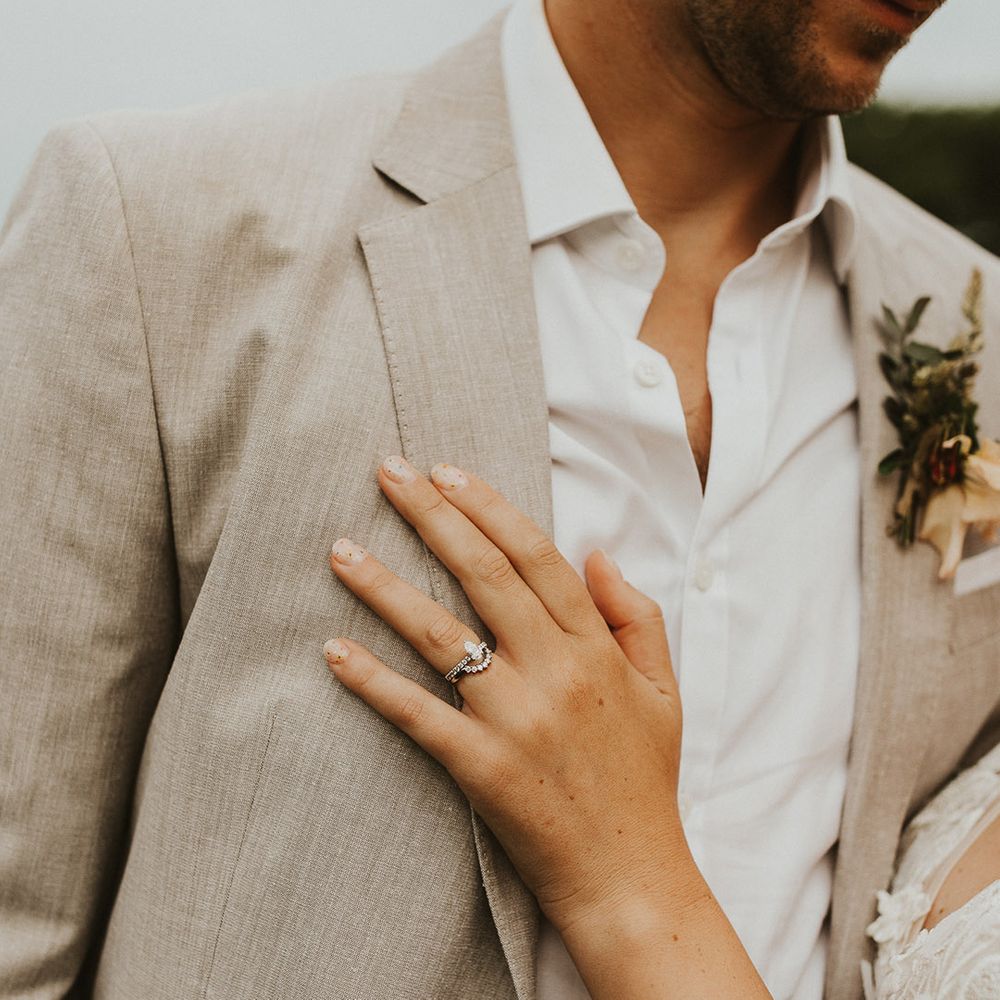 Bride's silver engagement ring and wedding band with colourful flower pattern nails with the groom in a light suit 
