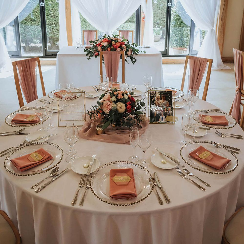 Circular wedding table with white tablecloth, pink wedding flower centrepiece and gold details 